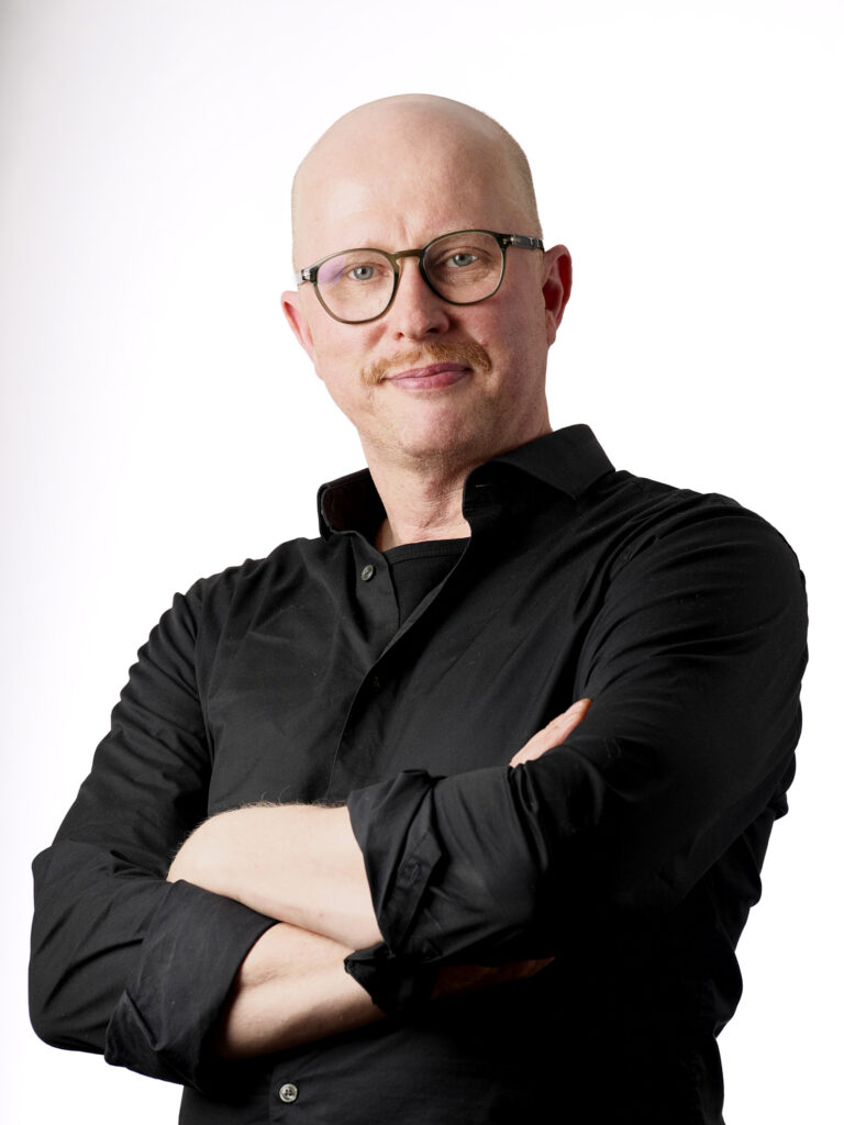 Kuva parturi-kampaaja Tuomaksesta poseeraamassa mustassa paidassa